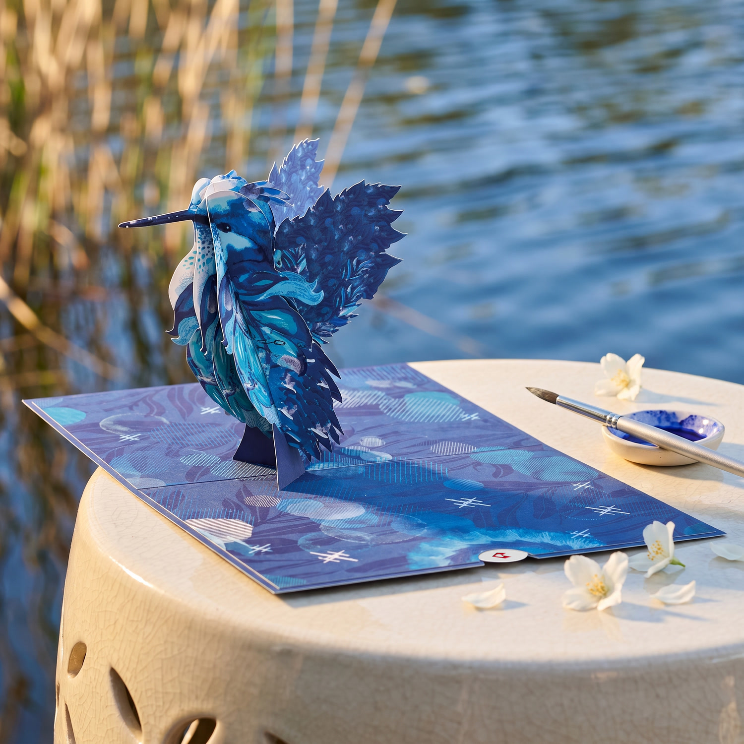 Blue hummingbird pop-up card beside a lake